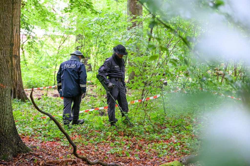 Polizeibeamte untersuchen mit einem Metalldetektor den in Planquadrate aufgeteilten Waldboden.