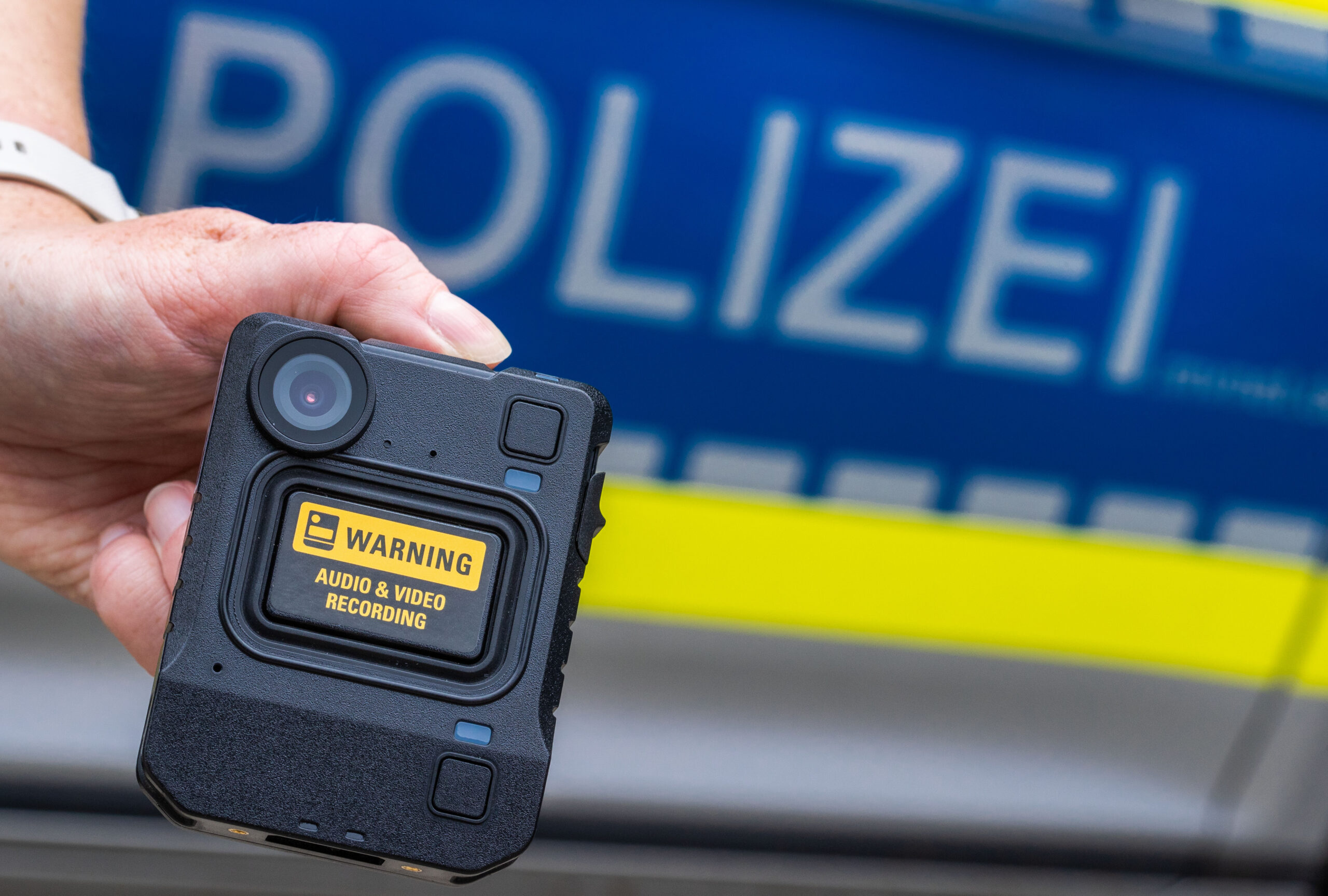 Eine neue Bodycam wird bei der Vorstellung des Systems vor einem Polizeiauto gehalten.