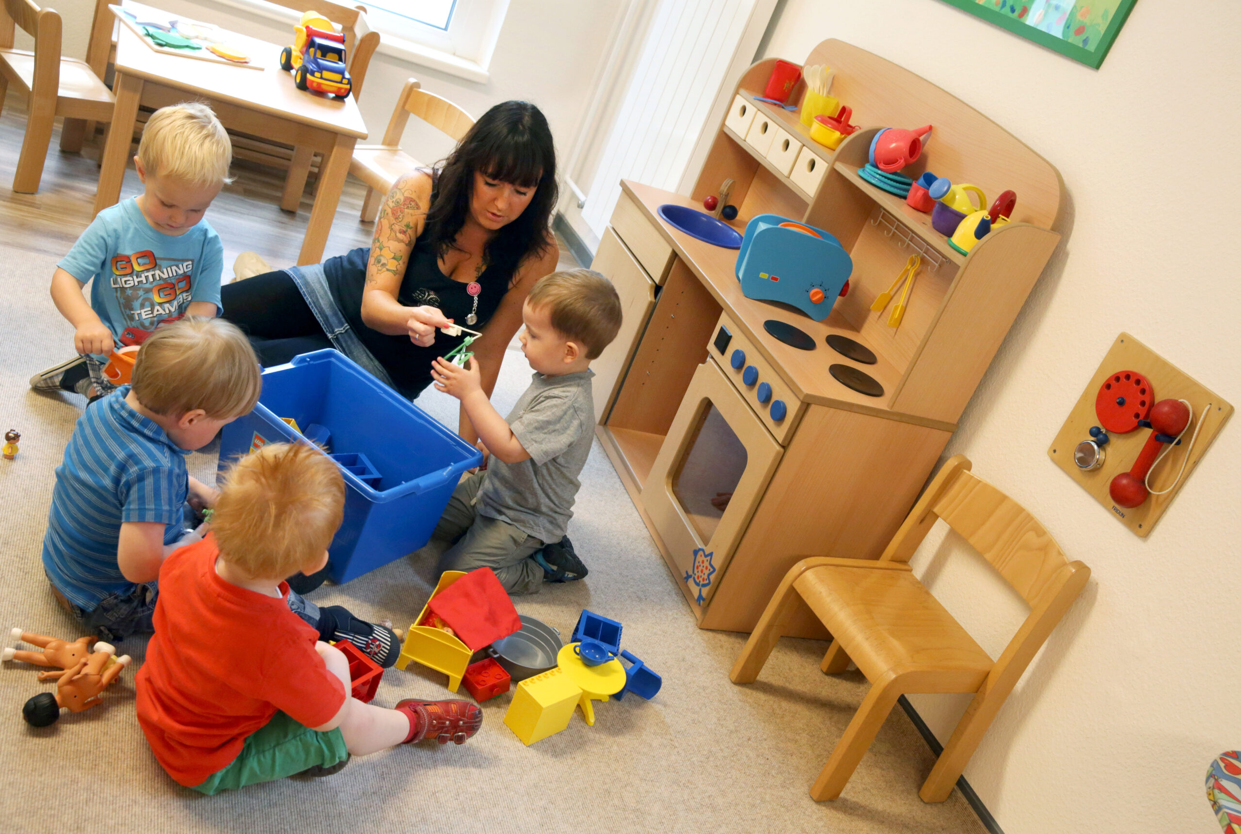 Erzieherin sitzt auf dem Fußboden und spielt mit vier Kindergarten-Kindern