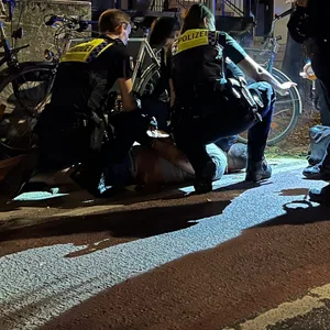 Polizisten fixieren den Mann am Boden und nehmen ihn fest.