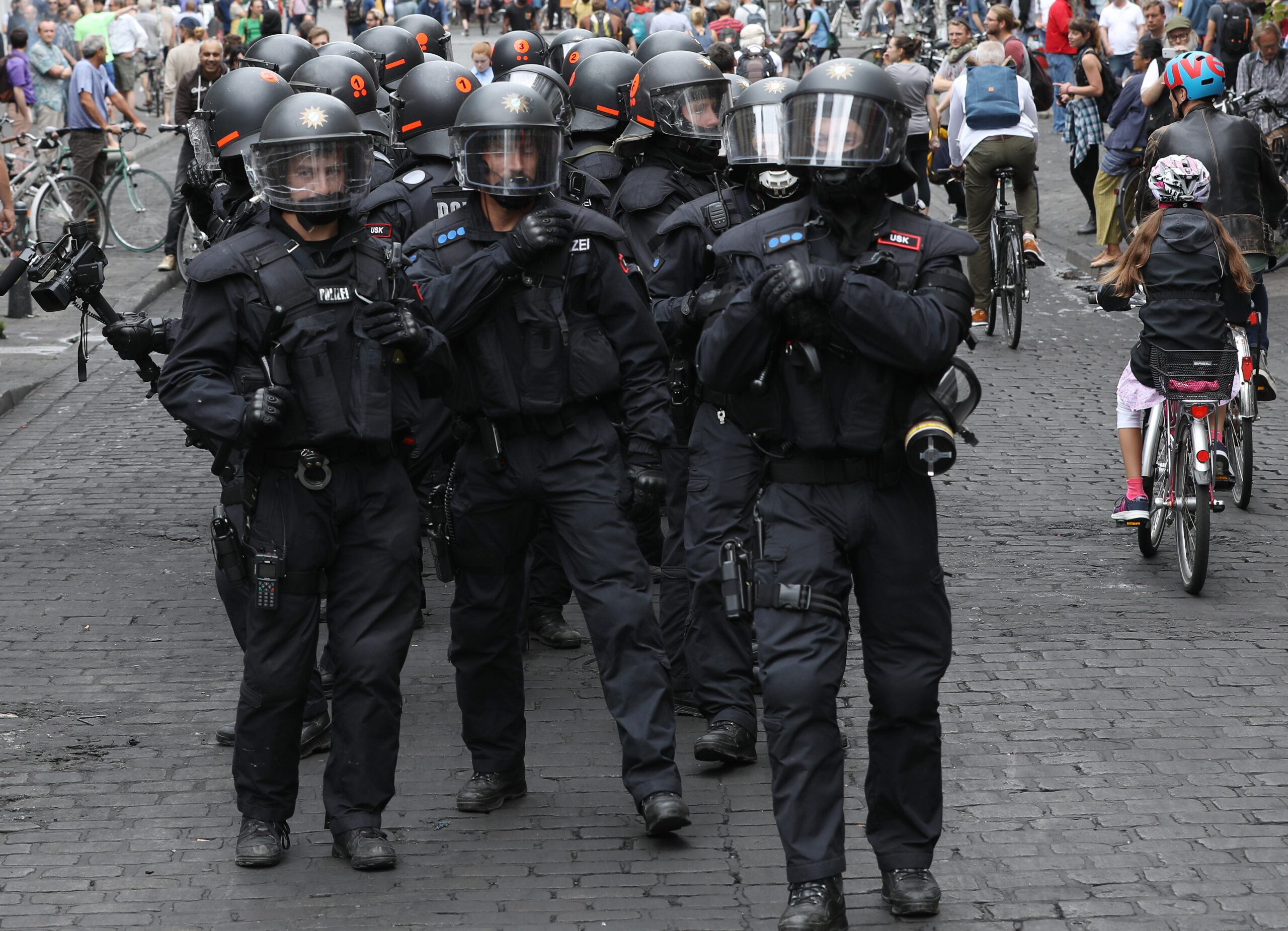 Polizisten mit Helmen gehen während des G20-Gipfels im Schanzenviertel zwischen Passanten und Radfahrern durch eine Straße. (Archivbild)