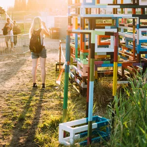 Drei Menschen stehen bei Sonnenuntergang vor einem Kunstwerk aus bunten Stangen und betrachten es.