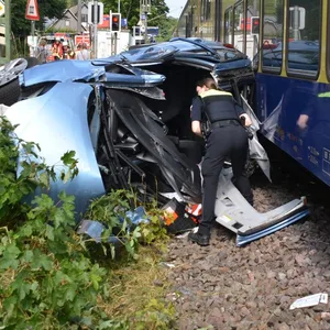 Eine Polizistin sieht in ein zerstörtes Auto, das neben dem Gleis liegt