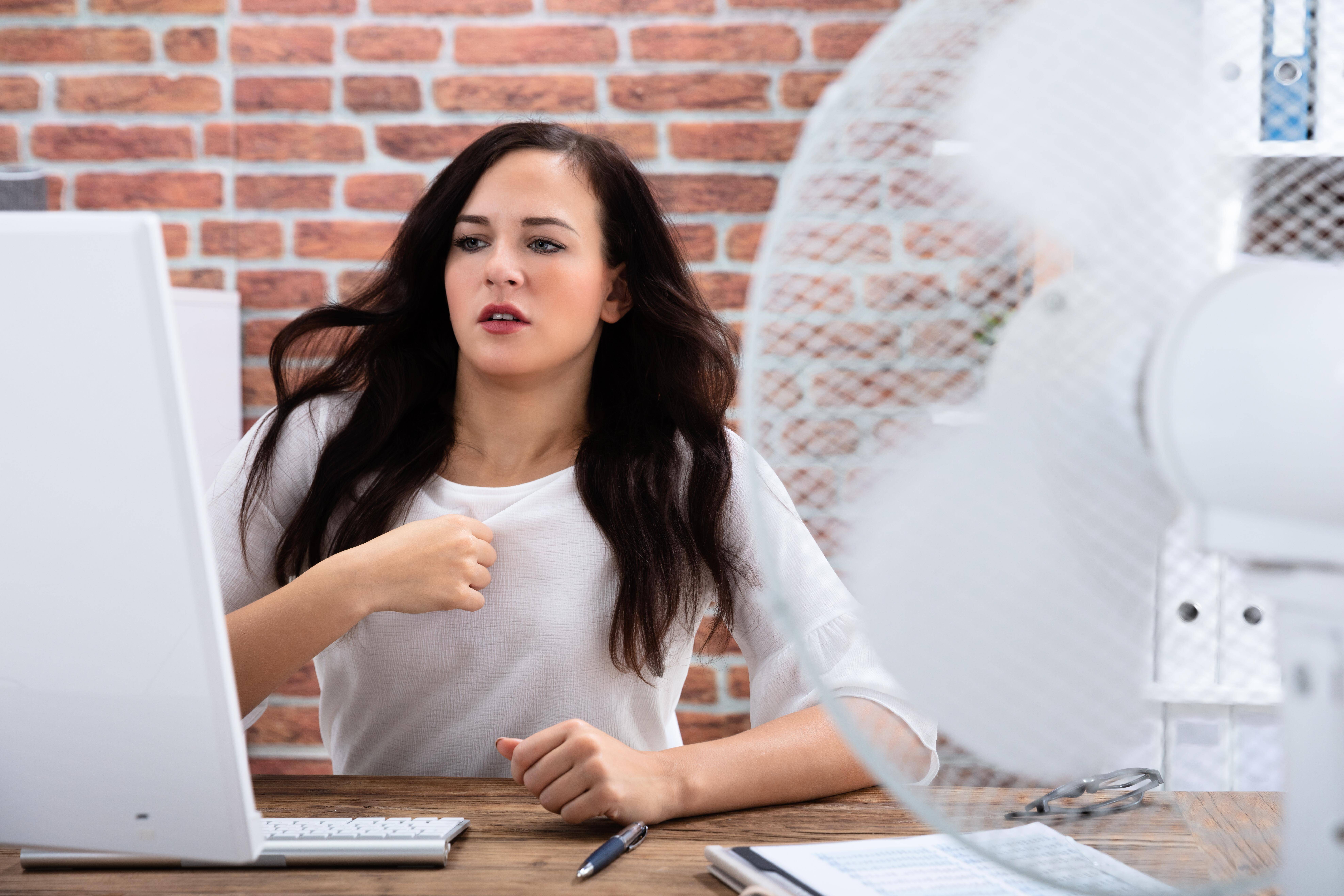 (Frau vor Ventilator in Büro) Es wird heiß – auch in den Büros. Eine Klimaanlage ist am Arbeitsplatz bisher nicht vorgeschrieben.