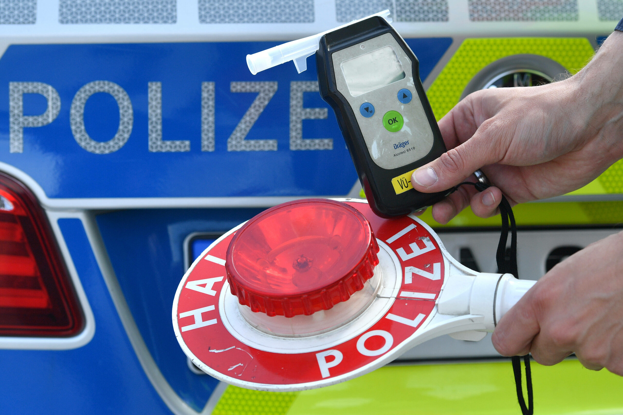 Eine Person hält vor einem Polizeiauto einen Alkoholtester vor eine Polizeikelle. (Symbolbild)