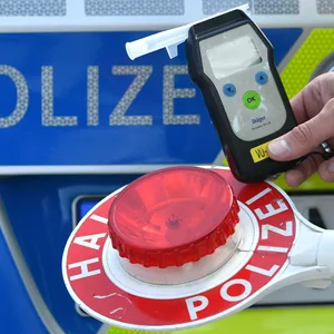 Eine Person hält vor einem Polizeiauto einen Alkoholtester vor eine Polizeikelle. (Symbolbild)