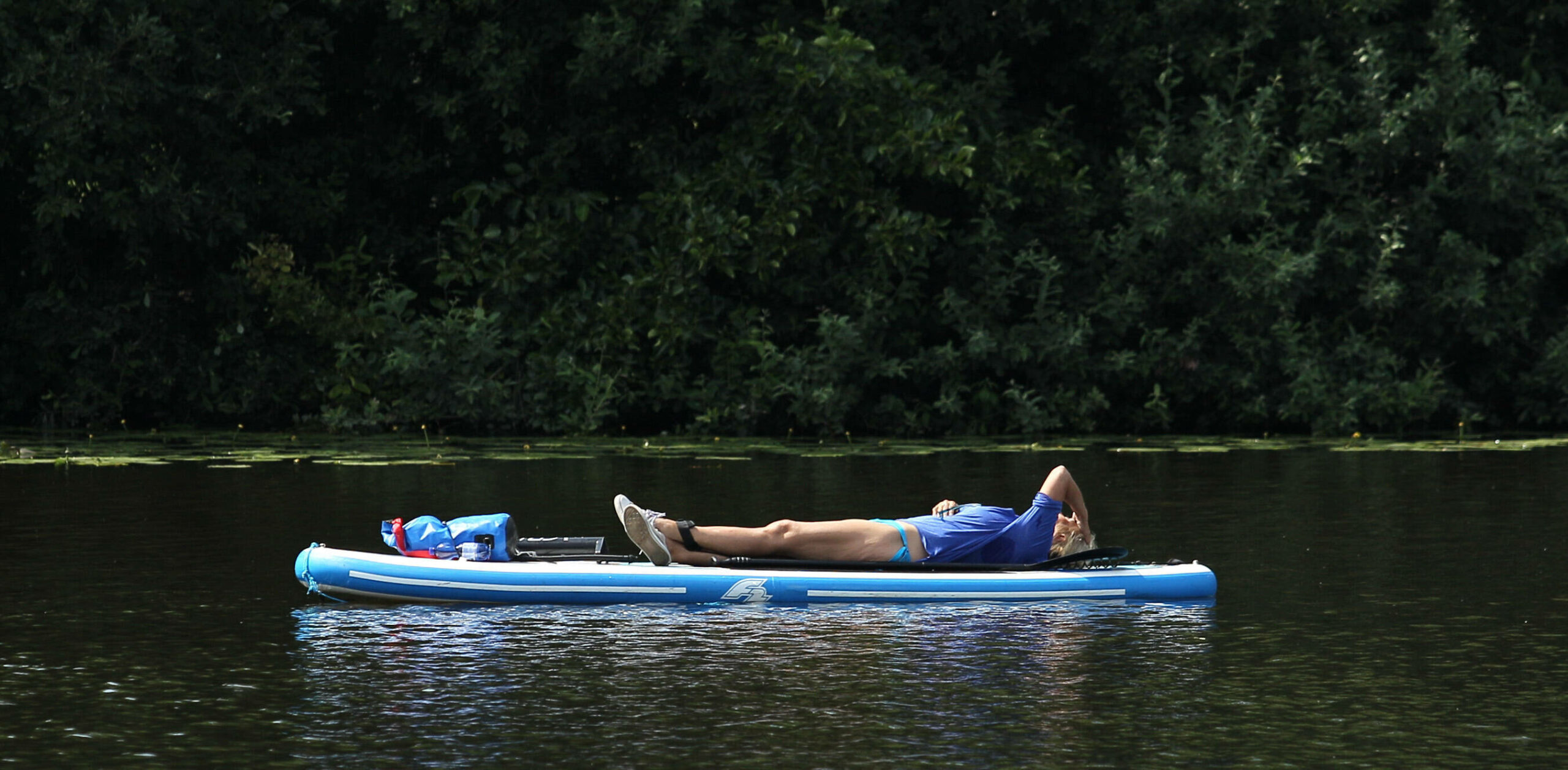 Was 'ne Hitze! Ein Mann liegt auf einem Stand-Up-Paddle-Board, das über einen Alsterkanal treibt.
