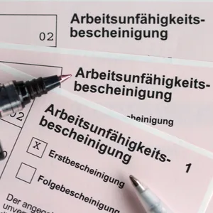 Stifte liegen auf den Arbeitsunfähigkeitsbescheinigungen für Arbeitnehmer:innen im Falle einer Krankschreibung durch Ärzte. (Symbolbild)