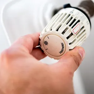 Ein Mann dreht am Thermostat einer Heizung.