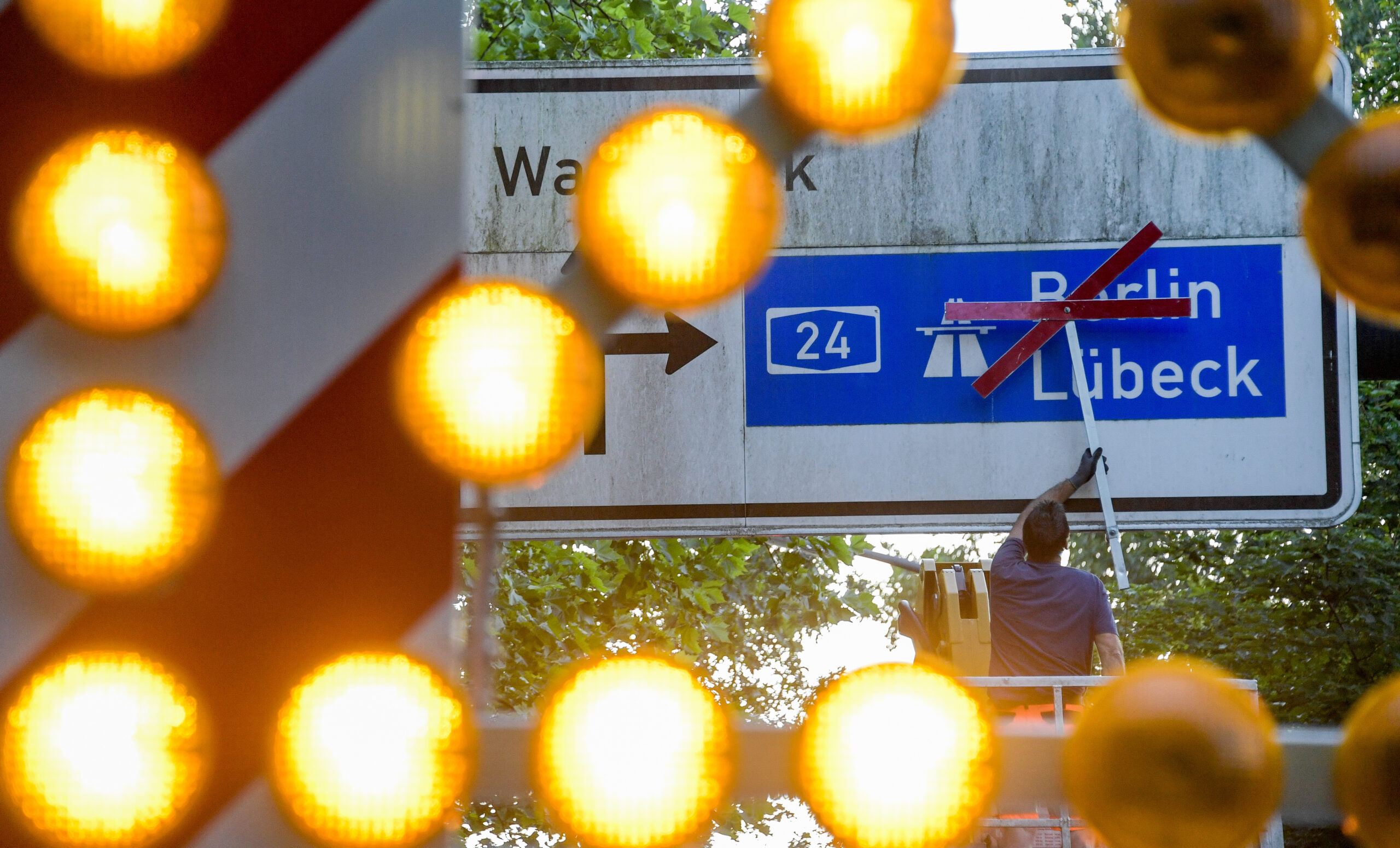 Ein Arbeiter befestigt rote Kreuze über den Richtungsschildern zur Autobahn A24.