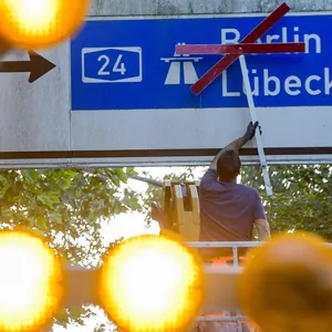 Ein Arbeiter befestigt rote Kreuze über den Richtungsschildern zur Autobahn A24.