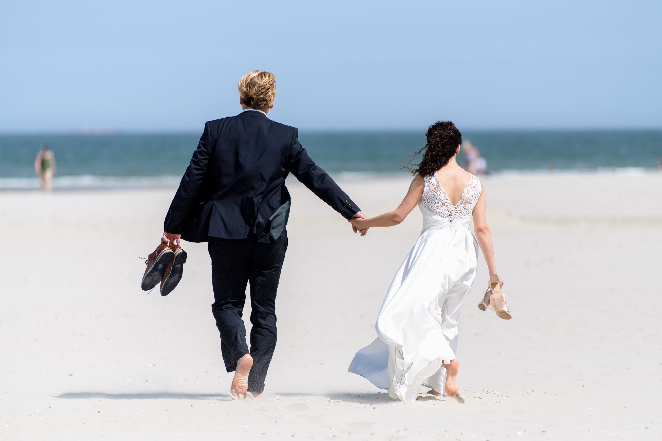 Ein Brautpaar geht nach ihrer Trauung am Strand entlang. (Symbolbild)