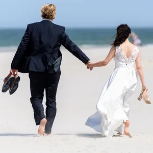 Ein Brautpaar geht nach ihrer Trauung am Strand entlang. (Symbolbild)