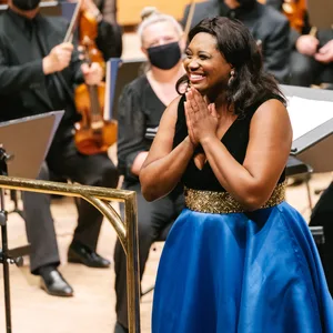 Die Sänger steht inmitten des Orchesters und legt die Hände wie zum Dank aneinander