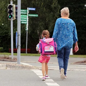 Ein Mädchen geht an der Seite einer Frau über eine Straße.