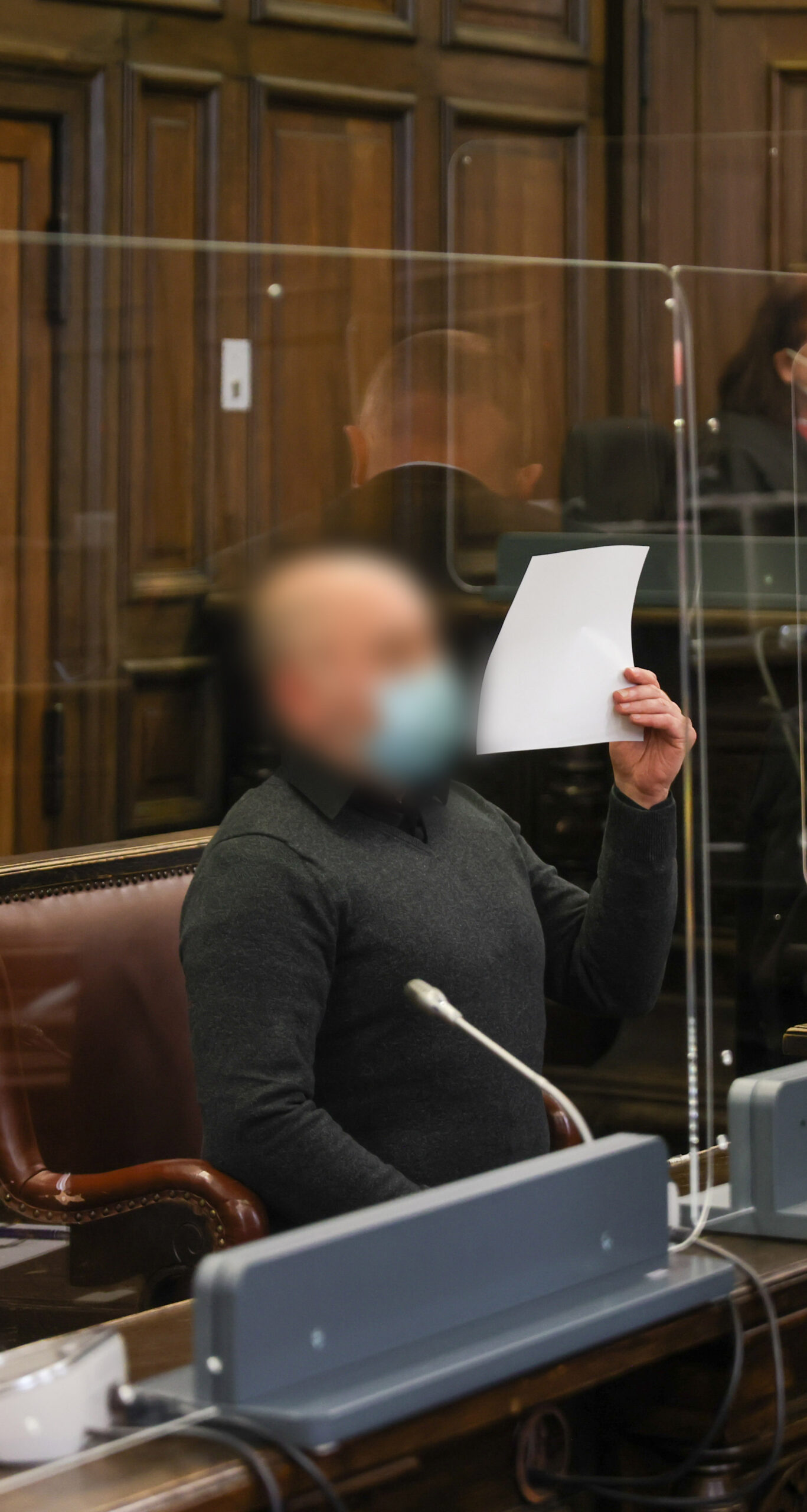 Angeklagte hält sich in einem Gerichtssaal des Strafjustizgebäudes in Hamburg ein Blatt Papier vor das Gesicht.