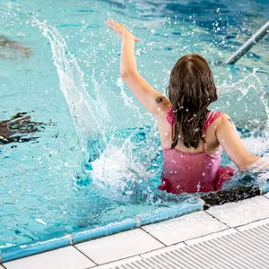 Ein Mädchen springt ins Wasser eines Schwimmbads.