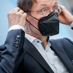 Lauterbach zieht sich eine schwarze FFP2-Maske über die Ohren