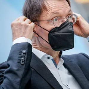 Lauterbach zieht sich eine schwarze FFP2-Maske über die Ohren