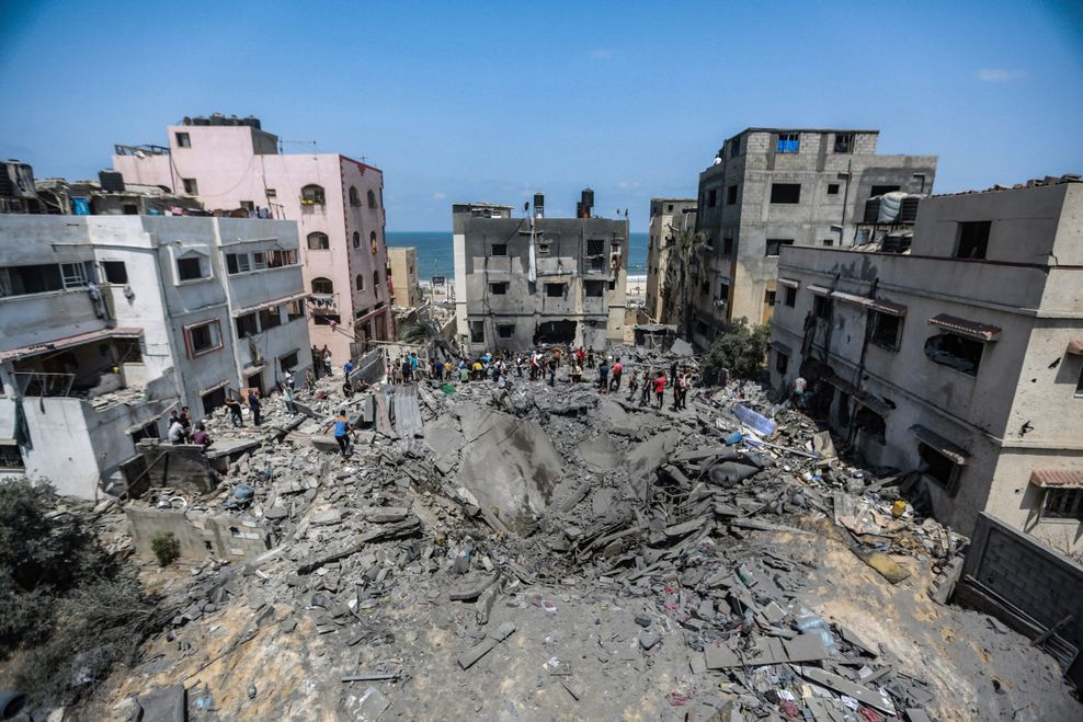 Palästinenser stehen im Gazastreifen nach einem israelischen Luftangriff in den Trümmern eines zerstörten Gebäudes.