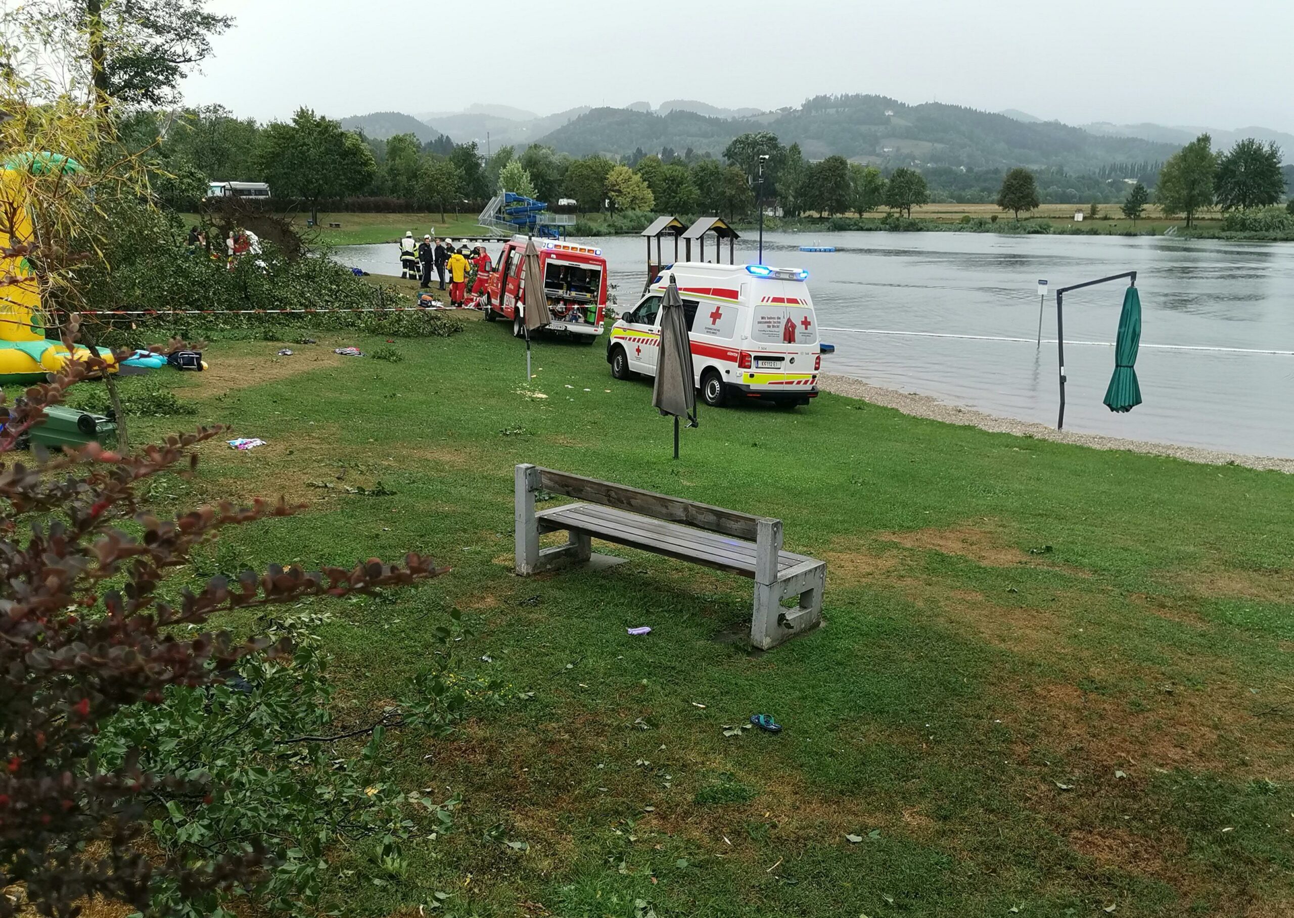 Rettungsfahrzeuge stehen neben umgekippten Bäumen an einer Unfallstelle am St. Andräer See. Bei einem schweren Unwetter, bei dem mehrere Bäume umgekippt sind, sind zwei Kinder gestorben und weitere Personen wurden teils schwer verletzt.