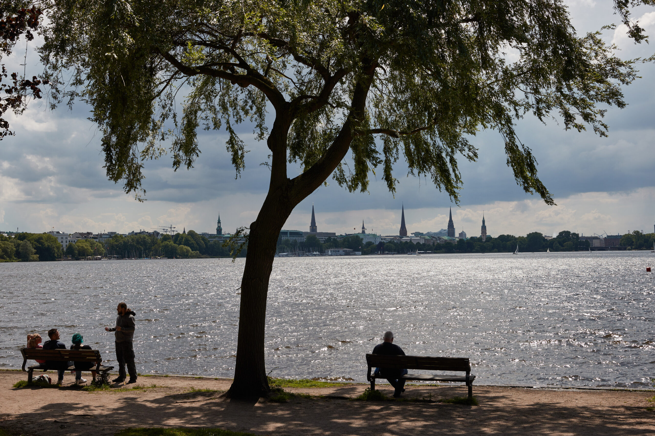 Menschen sitzen und stehen am Ufer der Außenalster. Die CDU in der Hamburgischen Bürgerschaft setzt sich für mehr Klönbänke in der Stadt ein.