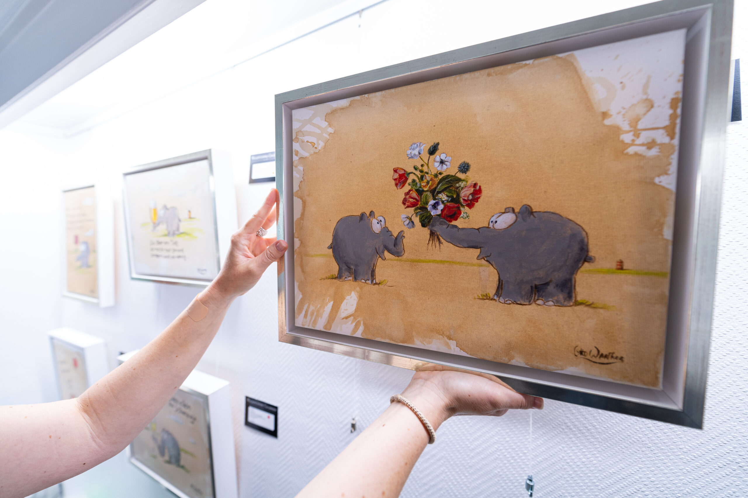 Eine Galeristin hängt in der Ausstellung ein Ottobild mit dem Titel „Lass Blumen sprechen“ an die Wand.