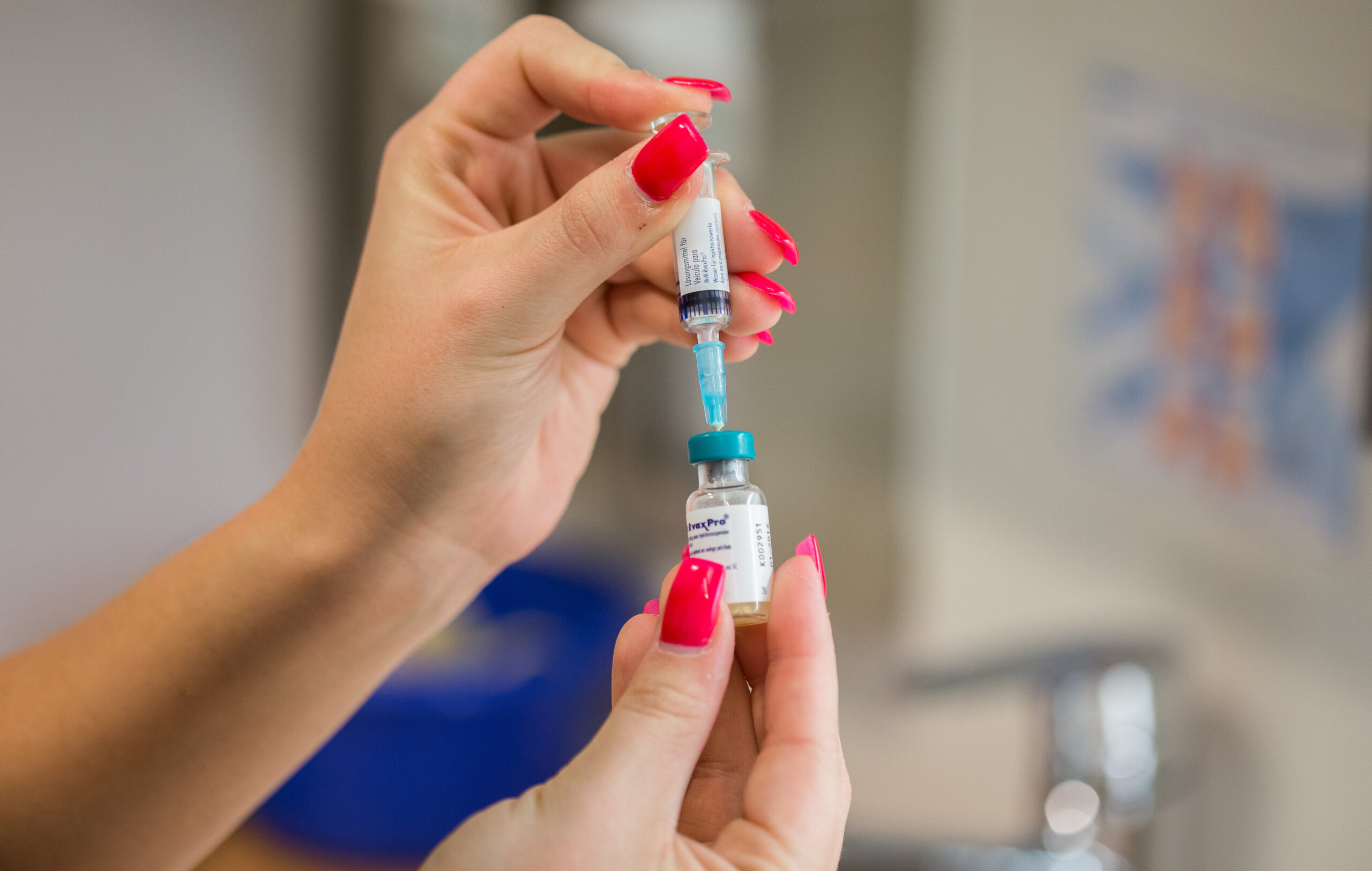 Eine Arzthelferin mit roten Fingernägeln bereitet eine Masernimpfung vor.