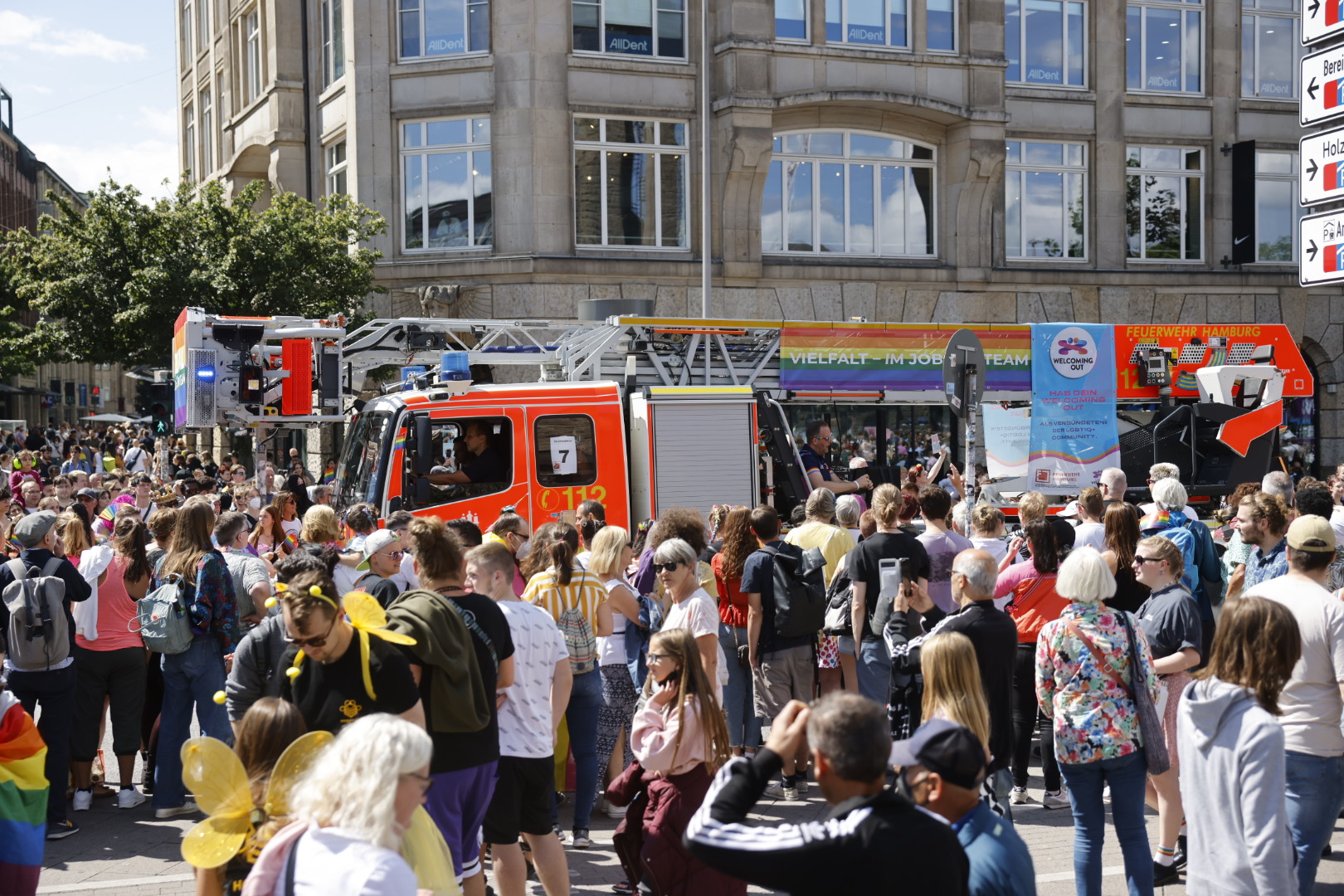 Ein Feuerwehrfahrzeug mit Regenbogenfahnen fährt zwischen einer Menschenmenge