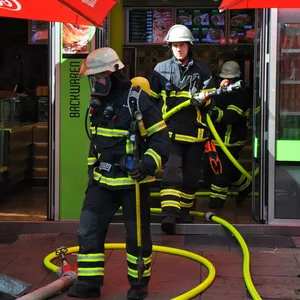 Einsatzkräfte der Feuerwehr treten aus einem Imbiss heraus