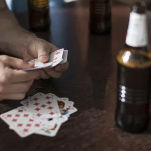 Ein Mann hält Spielkarten in der Hand, auf dem Tisch Bierflaschen