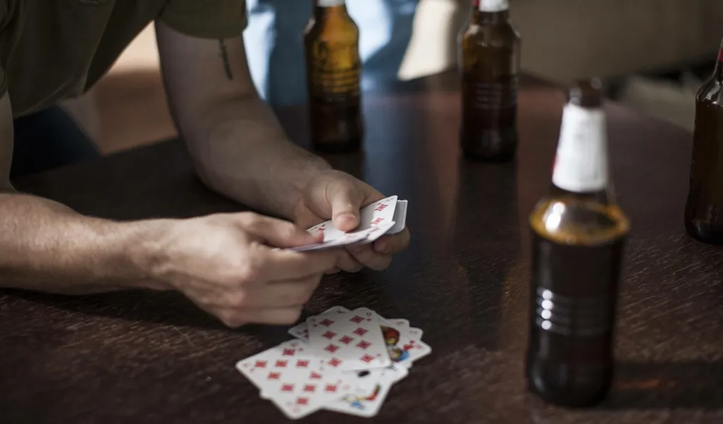 Ein Mann hält Spielkarten in der Hand, auf dem Tisch Bierflaschen