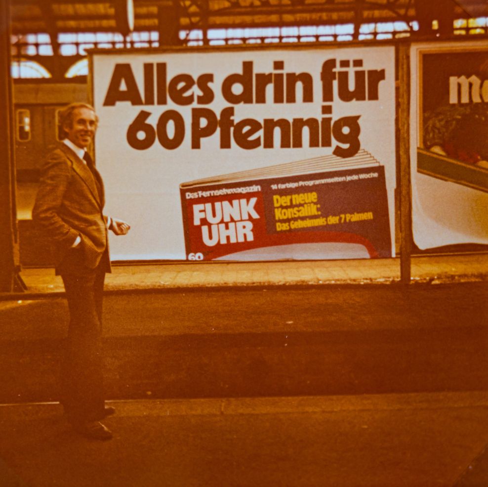 Wolfgang Rompa 1977 auf einem Bahnsteig vor einer Werbung für „seine Funk Uhr“