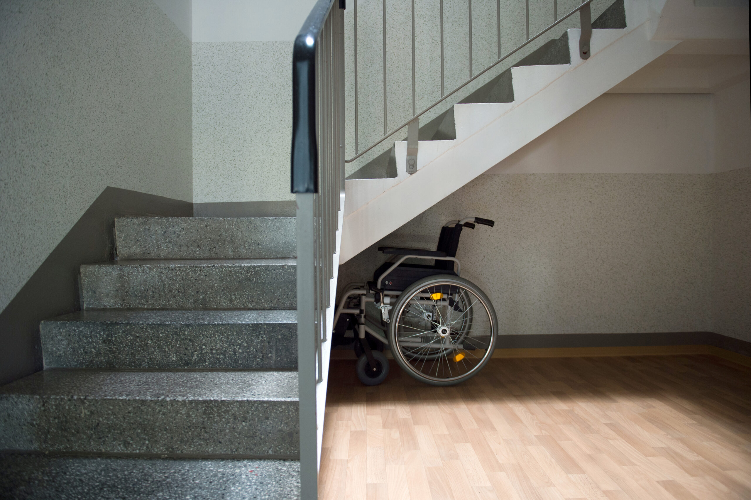Ein Rollstuhl steht unter einer Treppe.