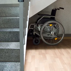 Ein Rollstuhl steht unter einer Treppe.
