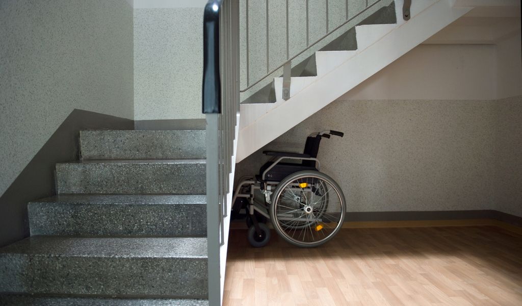 Ein Rollstuhl steht unter einer Treppe.