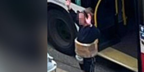 Ein Mann mit falschem Sprengstoffgürtel um den Bauch steht mit erhobenen Armen vor einem Bus