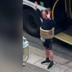 Ein Mann mit falschem Sprengstoffgürtel um den Bauch steht mit erhobenen Armen vor einem Bus