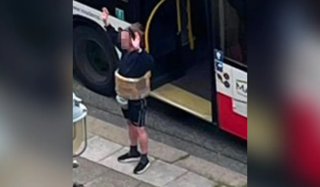 Ein Mann mit falschem Sprengstoffgürtel um den Bauch steht mit erhobenen Armen vor einem Bus