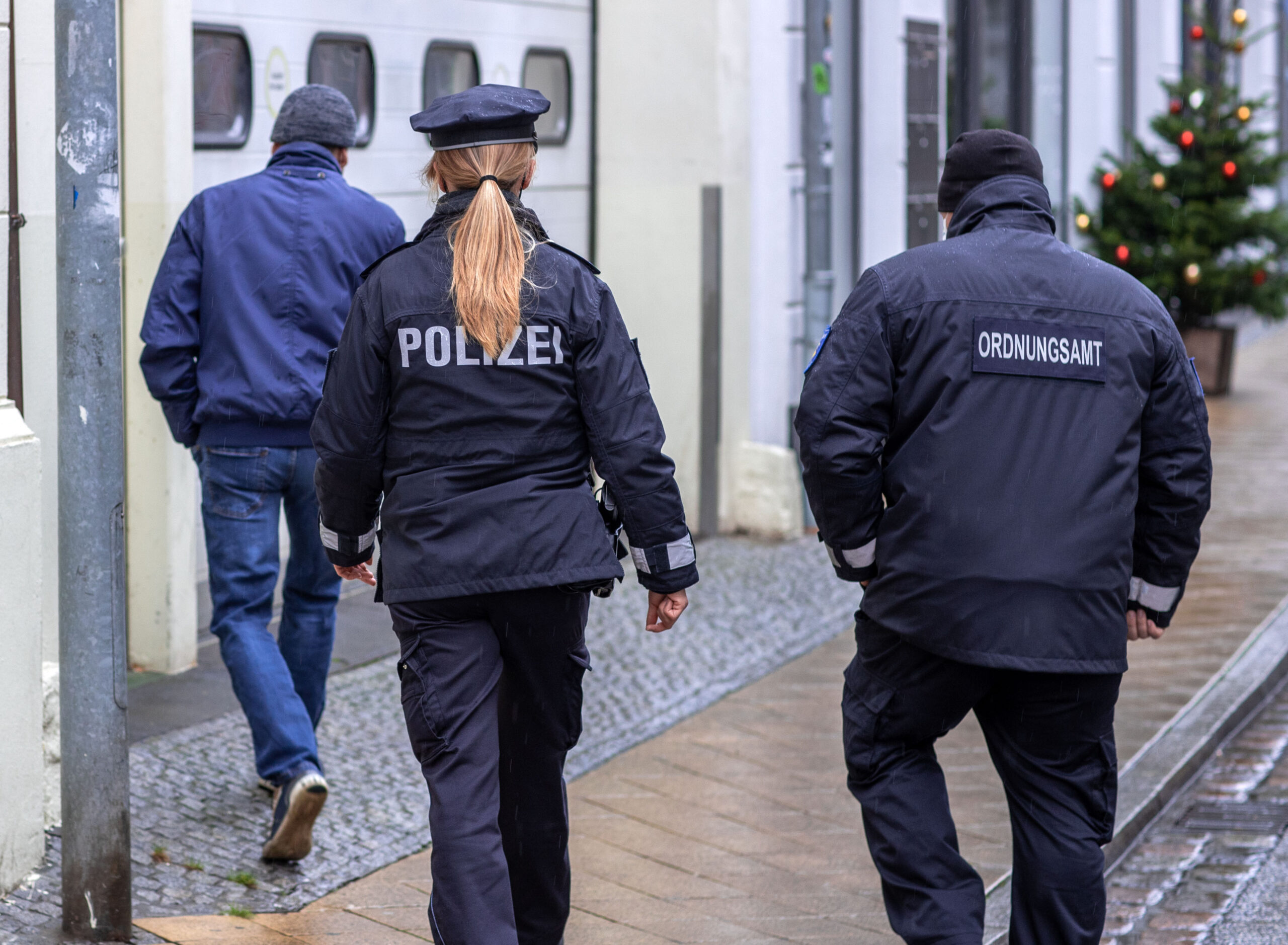 Eine Polizistin und ein Mitarbeiter des Ordnungsamtes folgen einem Passanten.