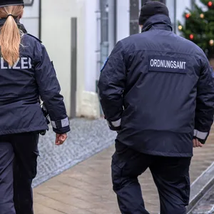 Eine Polizistin und ein Mitarbeiter des Ordnungsamtes folgen einem Passanten.