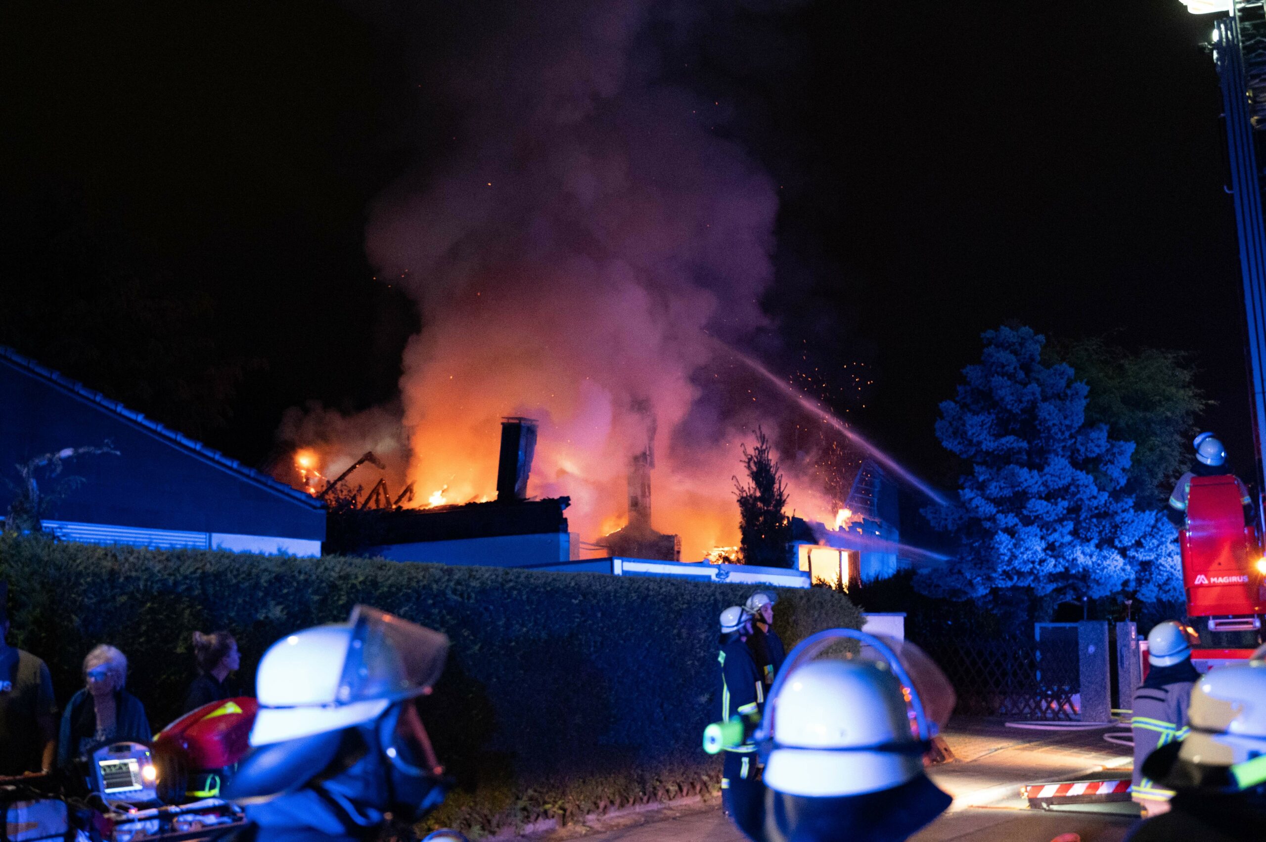 Einsatzkräfte der Feuerwehr stehen vor einem brennenden Haus.