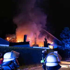 Einsatzkräfte der Feuerwehr stehen vor einem brennenden Haus.
