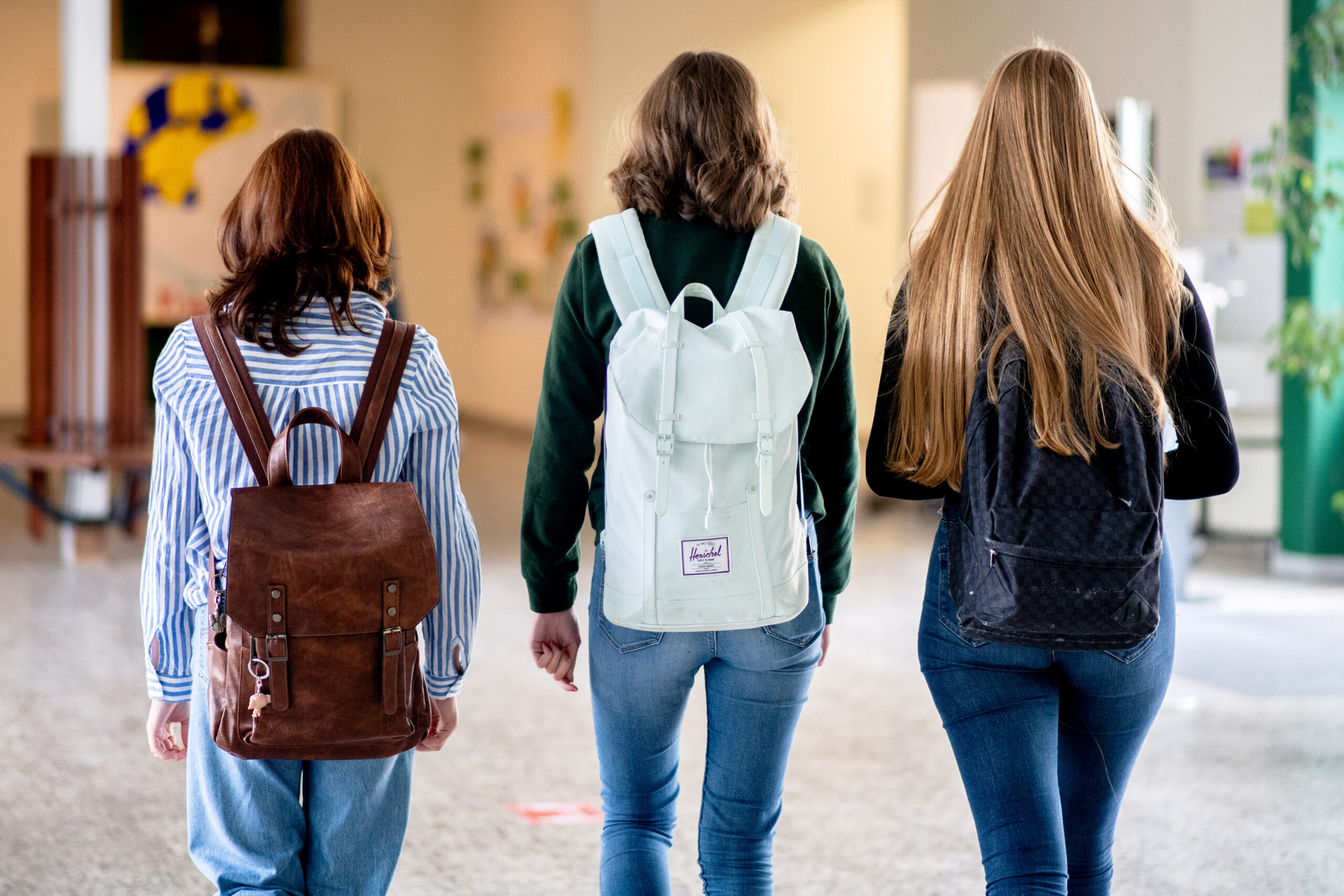 Drei Mädchen mit Rucksäcken auf den Rücken gehen durch eine Schule