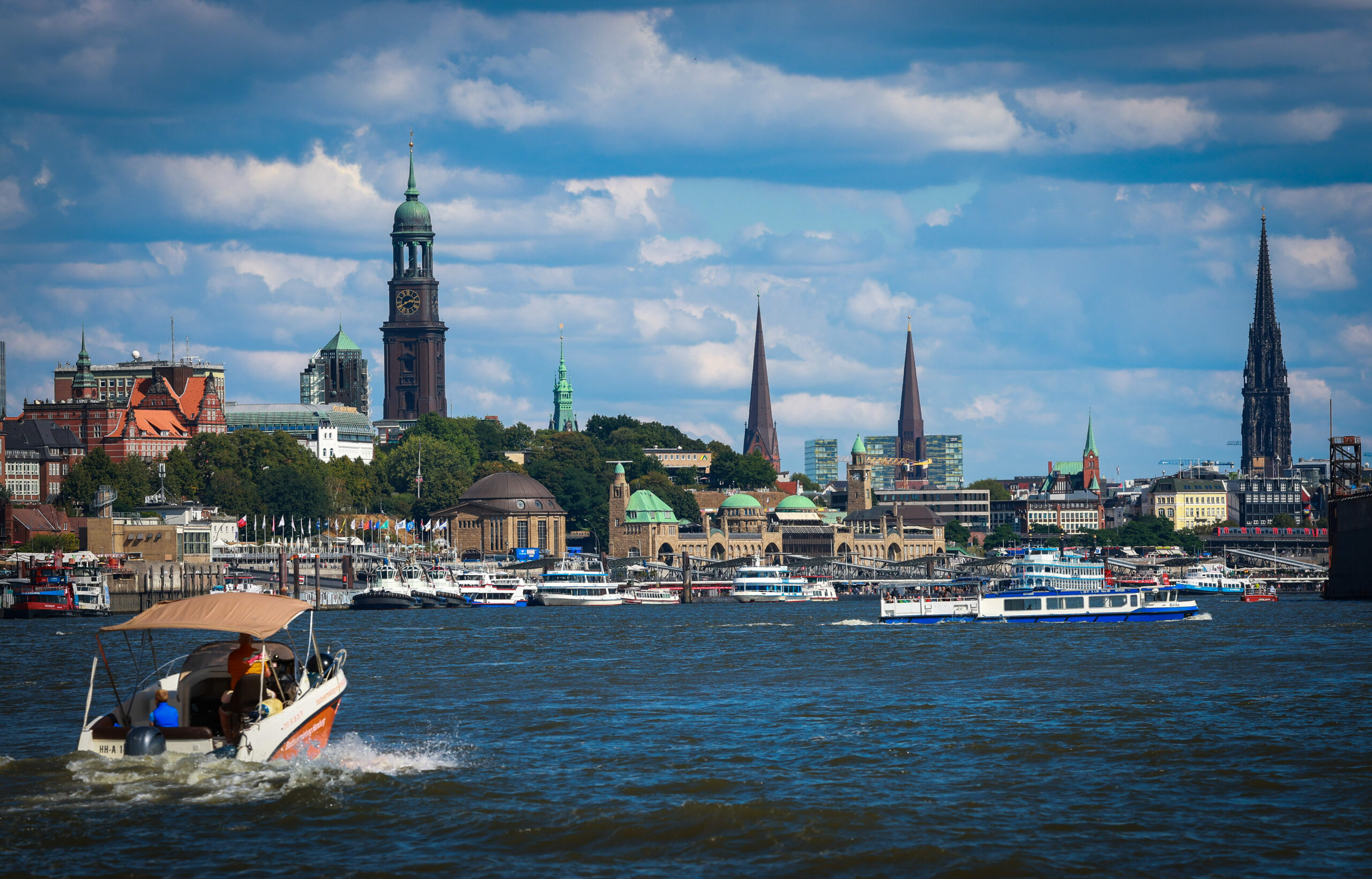 Zahlreiche Barkasse und Ausflugsschiffe liegen an den Landungsbrücken oder sind auf der Elbe vor der Skyline von Hamburg unterwegs.