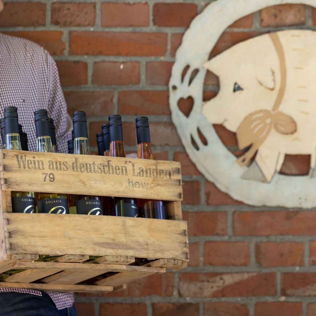 Der Landwirt Jan Brinkmann trägt eine Kiste („Wein aus deutschen Landen“) mit Weinflaschen aus seinem Hofladen.