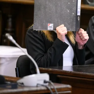 Die Angeklagte (l.) sitzt vor Beginn der Verhandlung im Gerichtssaal neben ihrem Verteidiger Dennis Grünert und verdeckt ihr Gesicht mit einem Aktenordner.