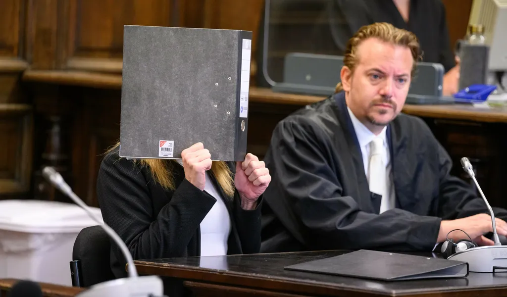Die Angeklagte (l.) sitzt vor Beginn der Verhandlung im Gerichtssaal neben ihrem Verteidiger Dennis Grünert und verdeckt ihr Gesicht mit einem Aktenordner.