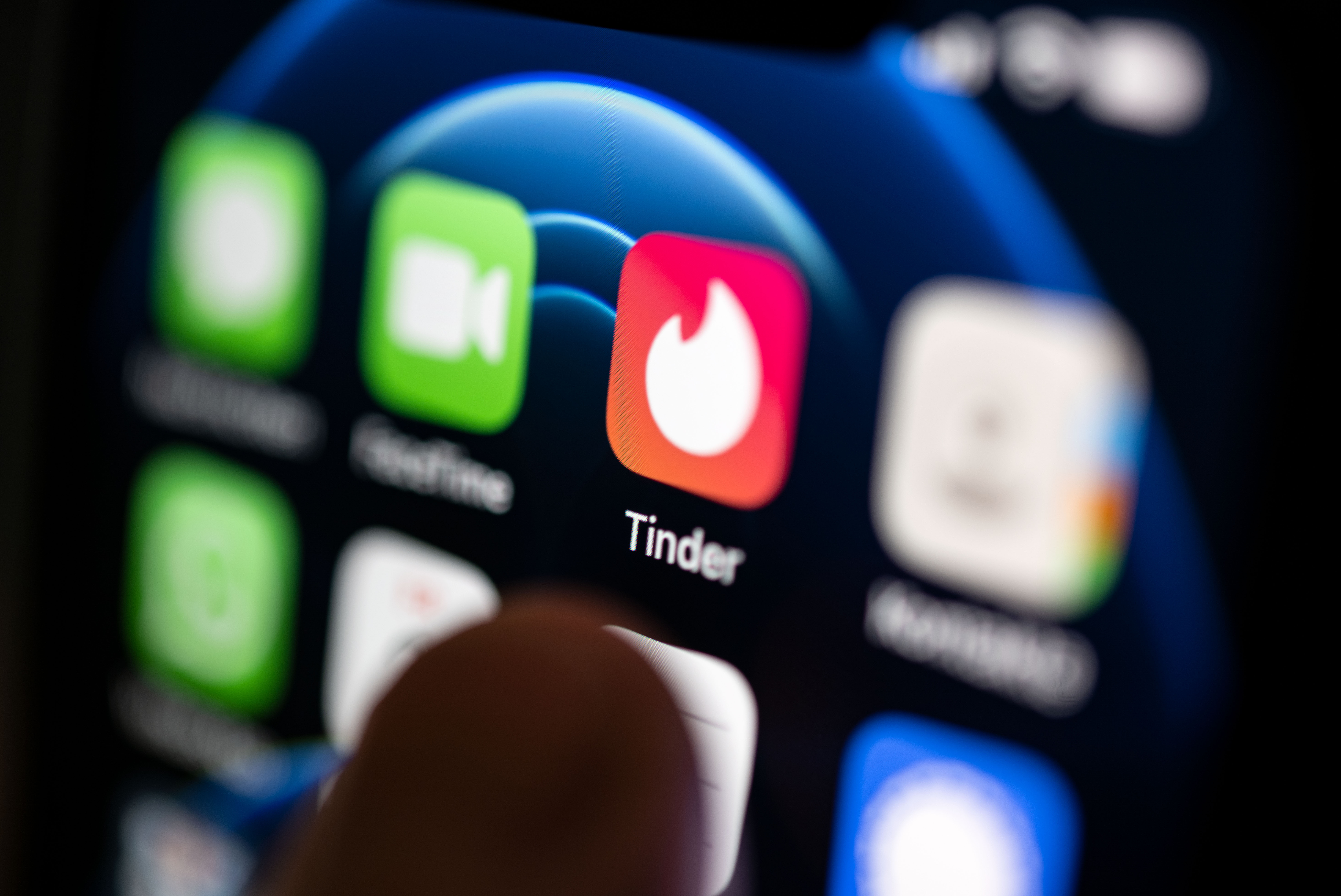 Eine Hand tippt auf die Tinder-App, die auf einem Smartphone installiert ist.