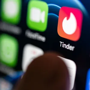 Eine Hand tippt auf die Tinder-App, die auf einem Smartphone installiert ist.